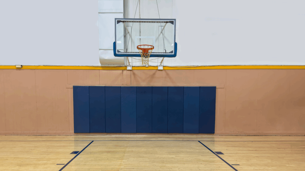 Indoor basketball court featuring a hoop, backboard, and padded wall, emphasizing design elements for functionality and safety.