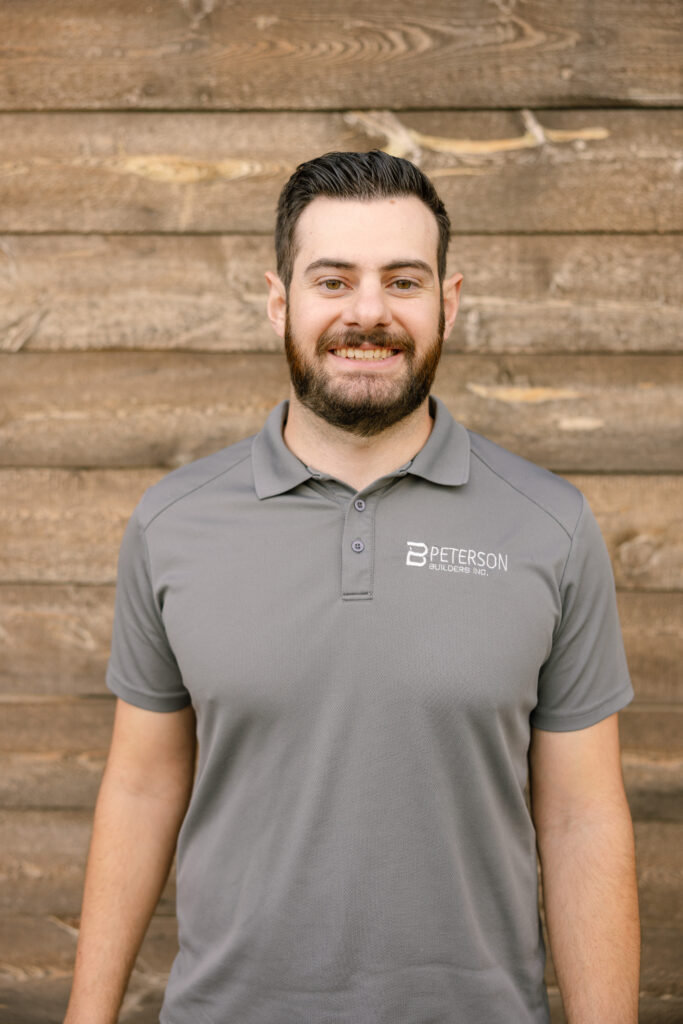 Jordan Adams, Warranty Manager at Peterson Builders, smiling in a gray polo shirt with the company logo against a wooden background.