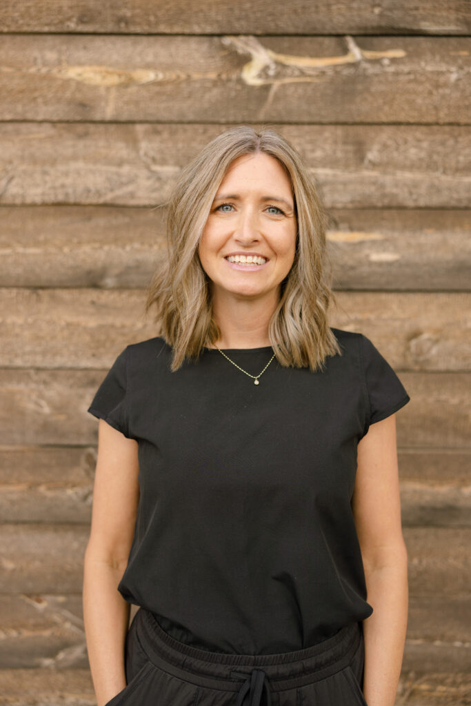 Kristen Peterson, Director of Finance at Peterson Builders, smiling in front of a wooden backdrop, showcasing her professional demeanor and connection to the Ogden, UT area.