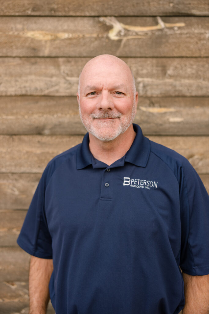 Marc Petty, Chief Operations Manager at Peterson Builders, smiling in a navy polo shirt with company logo against a wooden background.
