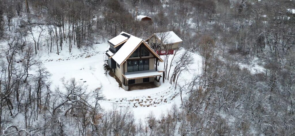 Aerial view of a custom luxury A-frame home surrounded by snow-covered trees in Northern Utah, showcasing craftsmanship and integration with the natural landscape.